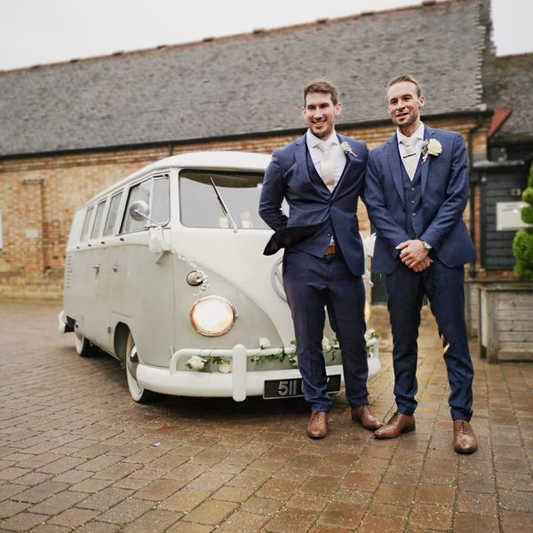 Groom poses for photos with his best man in front of a split screen camper