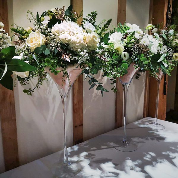 white flowers and foliage in four large martini glass style vases