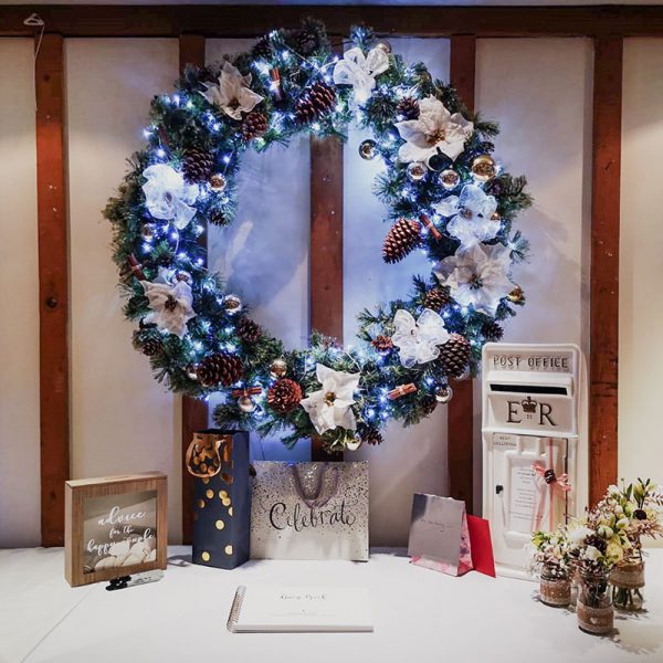 Wedding gift table with old fashioned white post box, floweres, gifts and a Christmas wreath with white poinsettias hanging above the table.