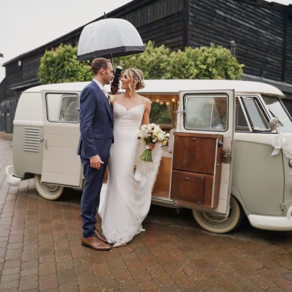 Bride and groom stand under an umbrella next to a 1961 VW camper