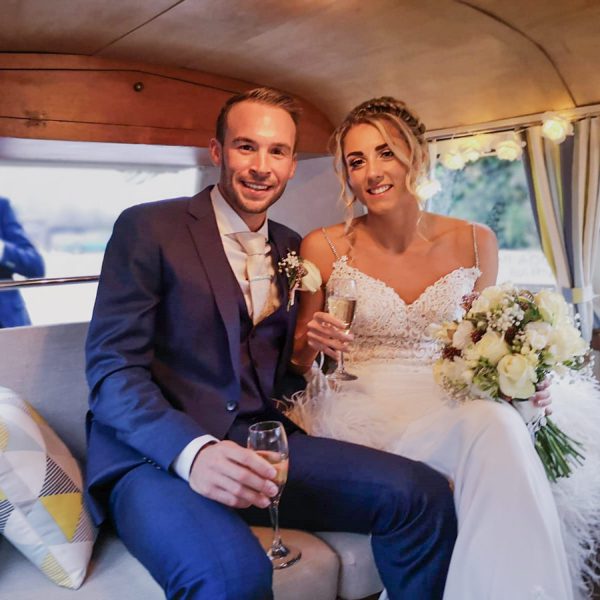 Bride and groom pose with glasses of champagne inside a vintage camper
