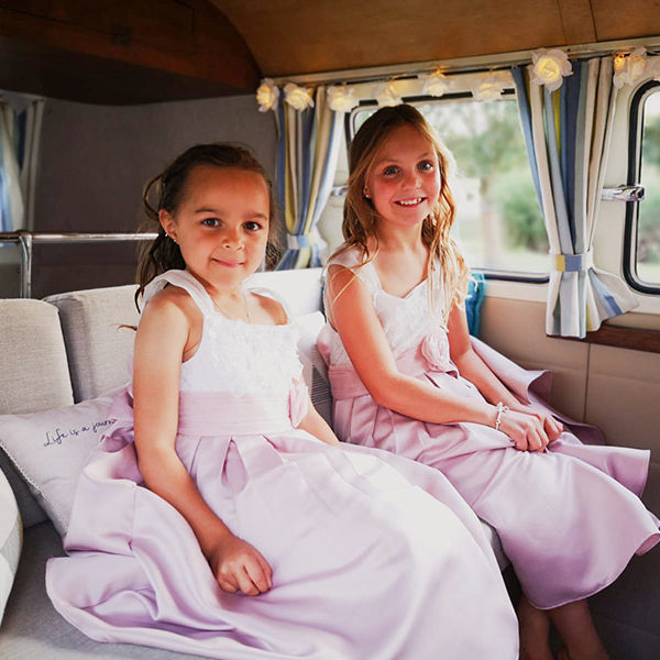 Flower girls in pink dresses sitting in the back of a classic VW campervan